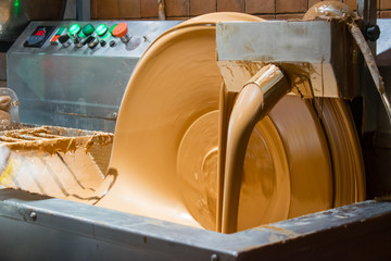 Chocolate tempering machine in action. Milk chocolate pouring down. Control panel on a background. 