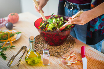 Anonymous lady in multicolored jacket mixing vegetables in bowl while cooking healthy salad in kitchen