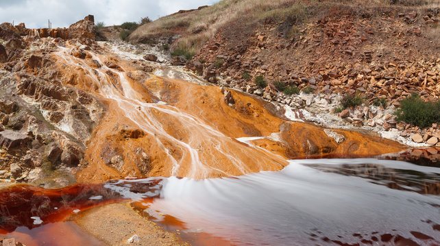 Small stream flowing on sandy rock on sunny day in long exposure in Mines of Riotinto, Huelva