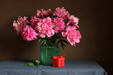 bouquet of pink peonies and a gift on the table. congratulations on the holiday.