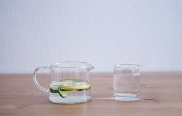 jug of lemonade and water sliced cucumbers and lemon on wooden table close up with blurred background