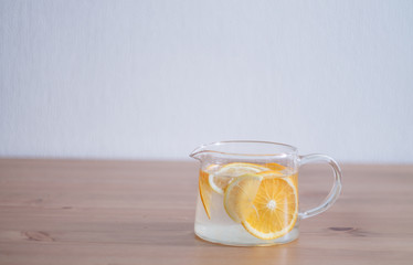 pitcher with lemonade and water sliced oranges and lemon on wooden table and coral and blue table background close up with blurred background