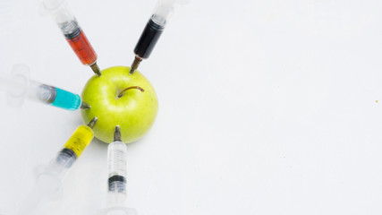 Pesticides, nitrates, gmo and other chemicals are injected into a green apple with syringes.