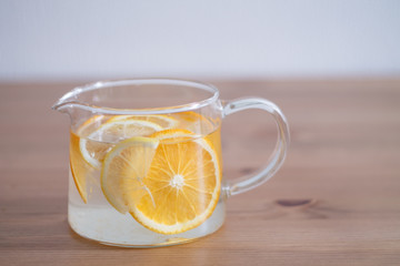 pitcher with lemonade and water sliced oranges and lemon on wooden table and coral and blue table background close up with blurred background
