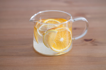 pitcher with lemonade and water sliced oranges and lemon on wooden table and coral and blue table background close up with blurred background