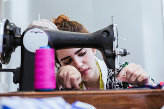 Teenage girl student practicing sewing on modern machine in cozy workshop
