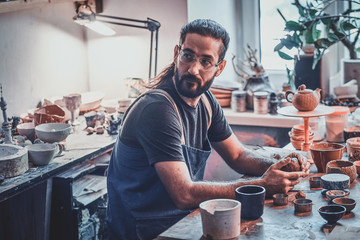 Diligent pensive man in glasses at his pottery workshop is workig for new project.