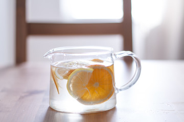 pitcher with lemonade and water sliced oranges and lemon on wooden table and coral and blue table background close up with blurred background