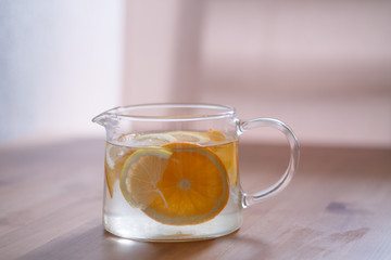 pitcher with lemonade and water sliced oranges and lemon on wooden table and coral and blue table background close up with blurred background