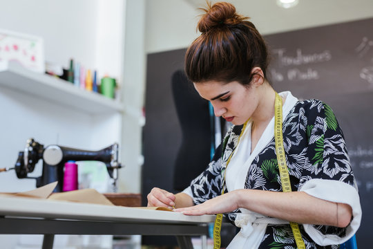 Teenage girl student practicing sewing on modern machine in cozy workshop
