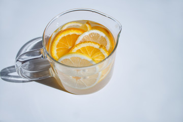 pitcher with lemonade and water sliced oranges and lemon on white table close-up with blurred background