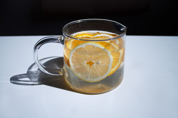 pitcher with lemonade and water sliced oranges and lemon on white table close-up with blurred background