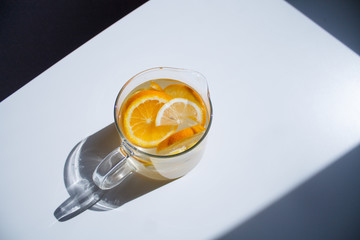 pitcher with lemonade and water sliced oranges and lemon on white table close-up with blurred background