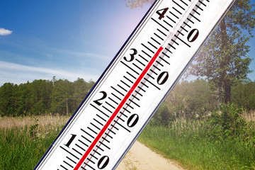 Thermometer showing high temperature isolated on blurry summer sunlight landscape.