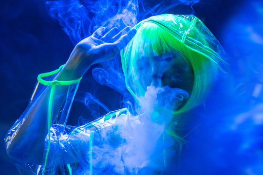 Young pretty unusual Asian woman in plastic transparent raincoat and yellow hair smoking in fluorescent light
