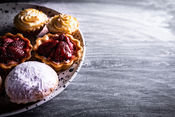 Muffins with cream and fruits, appetizing cupcakes on a dark background