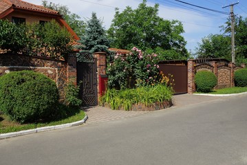 brown fence and gate on the street with green vegetation and flower bed along the asphalt road