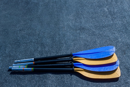 Blue And Yellow Paddle Blades On The Gray Textured Background. Look From The Side