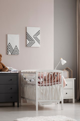 Vertical view of white crib with pastel pink bedding and cotton balls in grey and beige fashionable baby bedroom