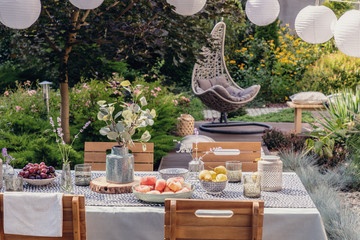 Table with flowers and food in the garden with hanging chair next to plants