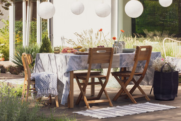 Rug next to wooden chairs at table with food on the terrace with lamps and flowers