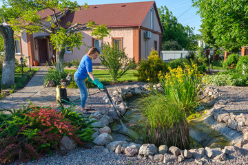 middle aged white woman cleans artificial pond with high-pressure wash from sludge.