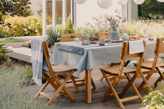 Wooden chairs at table with food and flowers on the terrace of house with plants