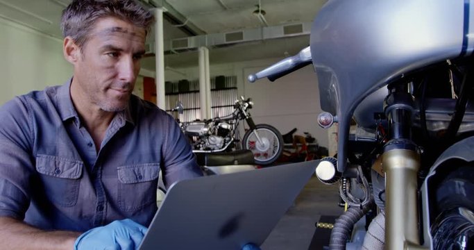 Male mechanic using laptop in motorbike repair garage.