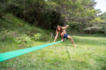  Defocused young man with naked torso doing slackline in field on summer day