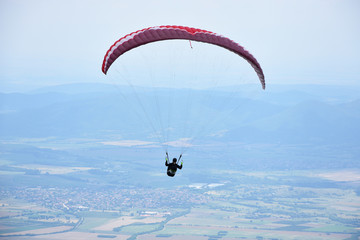 Young woman gliding in the sky above the town of Sopot, Bulgaria. Paragliding jump from the hills of Stara Planina Mountain. 