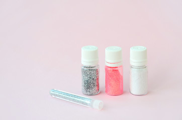 Colorful glitters lies on pastel pink background. Many round jars with multi-colored bright sparkles for nail polish