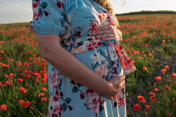 Pregnant young girl in the last month of pregnancy on the poppy field and supports the abdomen with...