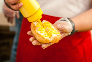 chef hands puts mustardon a hot dog bun
