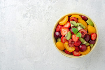 Healthy fresh fruit salad in bowl on gray concrete background. Top view. Copy space.