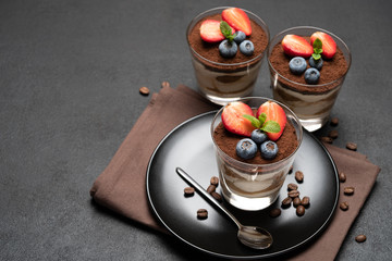 Classic tiramisu dessert with blueberries and strawberries in a glass on stone serving board on dark concrete background