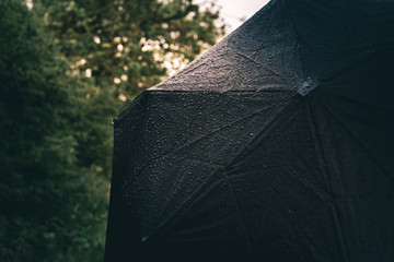 A dark black umbrella is wet with rain drops on it during a rain storm outside in a forest