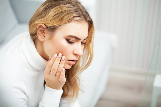 Pain. The problem of teeth. A woman feels pain in her tooth. A picture of a beautiful, sad girl suffering from severe pain in her teeth. An attractive woman feels painful toothache