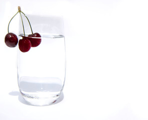 a glass cup with clean drinking water and three cherries on one branch on the edge. Glass with water and cherry on a white background. Copy space
