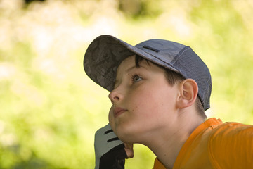 The boy is resting on a natural background, propping his cheek with his hand