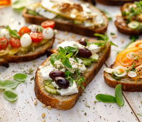 Open sandwich made of slices of sourdough bread with avocado, feta cheese, kalamata olives, olive oil and oregano on a wooden white table, close-up. Vegetarian food
