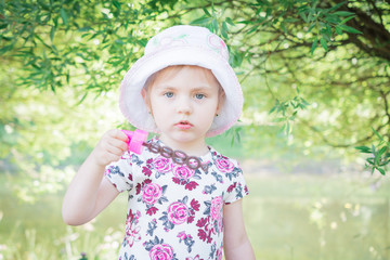 A little girl blowing soap bubbles in summer park