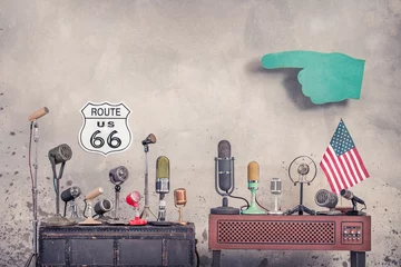 Fototapete Route 66 Retro old microphones for press conference or interview, USA flag, big pointing finger and historical road Route 66 sign front aged concrete wall background. Vintage style filtered photo  © BrAt82