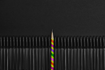 Row of dark black mechanical pencils with a real colorful pencil against a black copyspace background