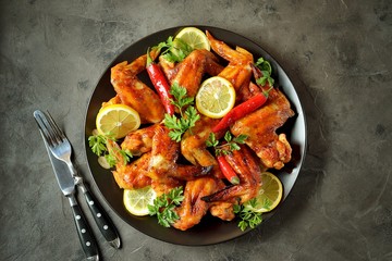 Delicious grilled chicken wings with lemon juice and chili pepper on black concrete background. Top view. 