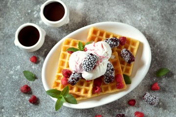 Belgian waffles with ice cream, mint and frozen raspberries and blackberries. Tasty breakfast.