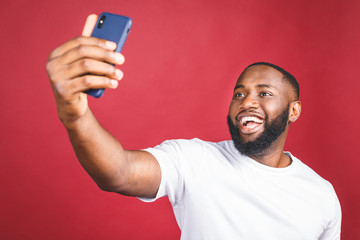Say cheese. Close up of young beautiful dark-skinned black man in casual smiling with teeth, holding smartphone, making selfie photo.