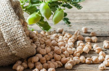 Uncooked dried chickpeas in burlap sack with raw green chickpea pod plant on wooden table. Heap of...