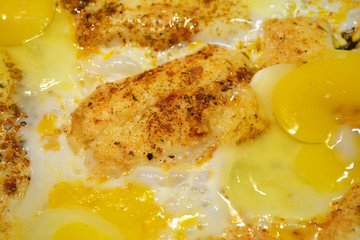 Close up view of the fried eggs on a frying pan. Salted, spiced and  with cheese and fried bread surface background