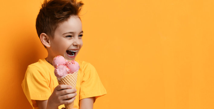 Baby boy kid hold strawberry pink ice-cream in waffle cone happy laughing looking at the corner on yellow