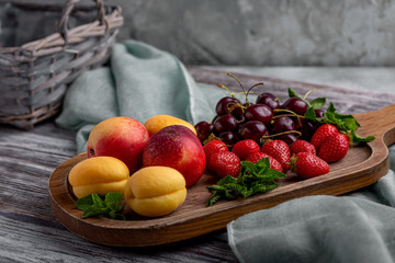 Healthy fruit platter, strawberries, apples, peaches, apricots on a dark gray wooden table, top view, close-up, selective focus.